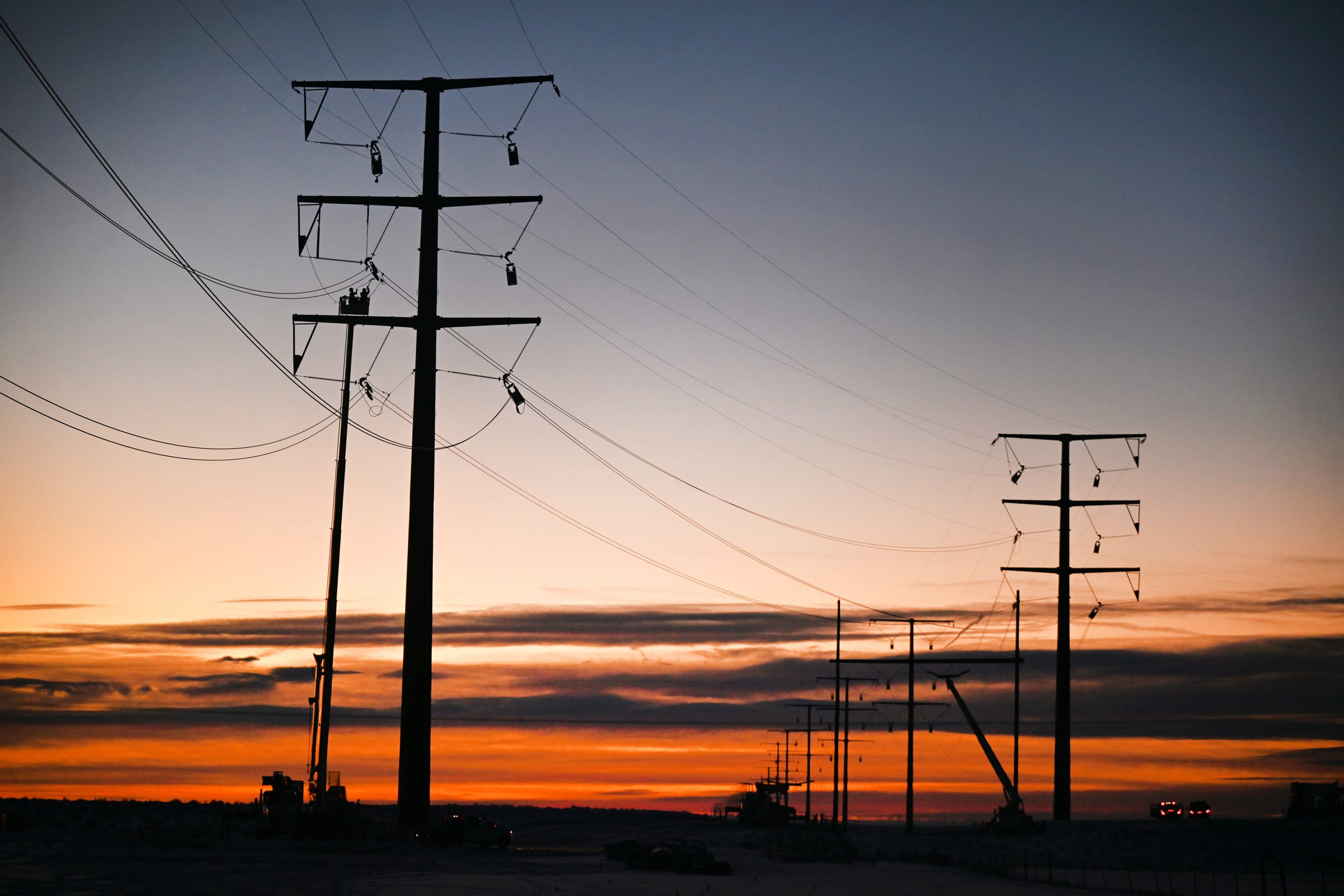 Line workers silhouetted on distribution poles at dusk
